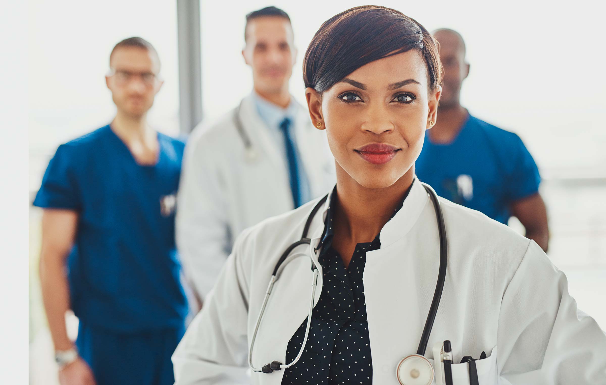 Black female doctor in foreground facing camera with male doctors stand in distance behind her