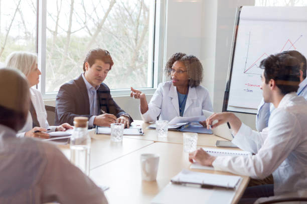 Mature female doctor gestures while discussing something during a healthcare conference with colleagues.