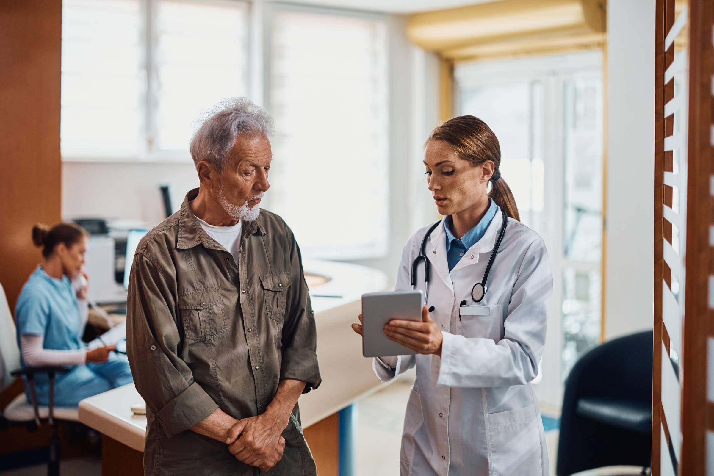 General practitioner and her senior patient using digital tablet at doctor's office.